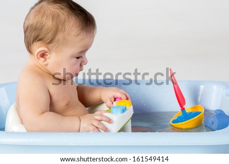 Baby boy bathes in a bathtube with toy boat
