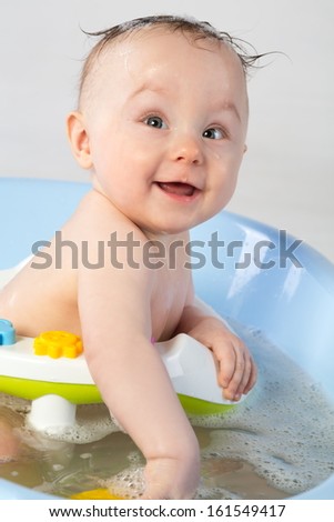 Smiling baby girl in a bathtube with toys
