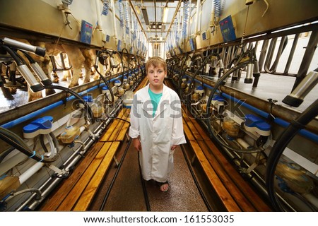 Boy in white robe and many machines for milking of cows in big farm.
