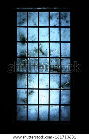 Big old dirty window with blue scratched glasses in dark room.