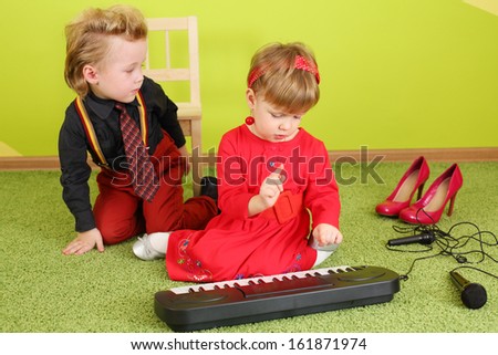 Little girl and boy in bright clothes sitting on the floor near the children piano