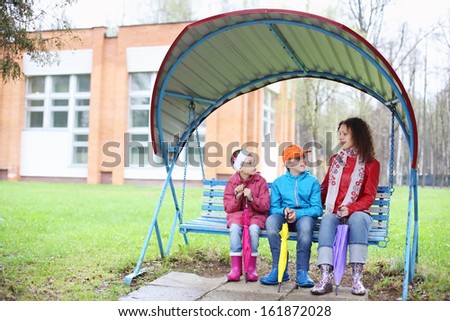 A mother and two children sitting on a swing on a cloudy day