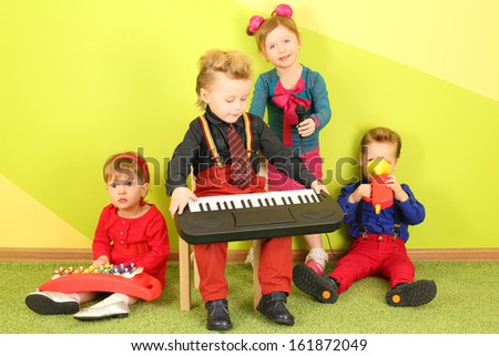 Four children with microphone and musical instruments: toy piano, metallophone and toy trumpet