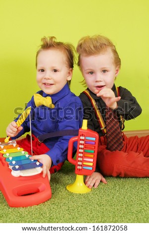 Two boys are sitting back to back with children trumpet and metallophone
