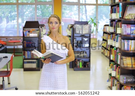 A pensive woman standing in the middle of the book room with a big book