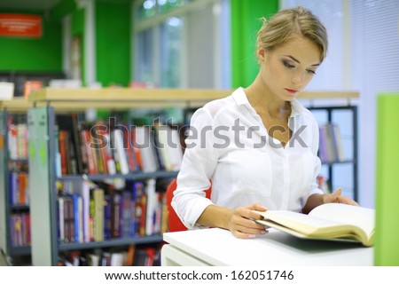 A young woman reading a book in the reading room of the library