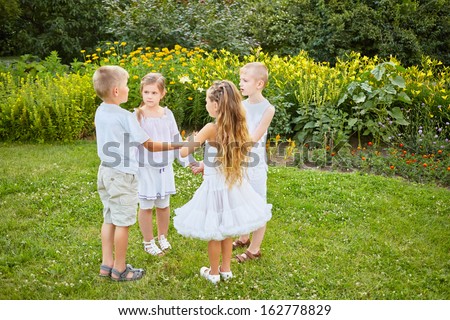 Four children stand in circle holding hands on grassy lawn in summer park