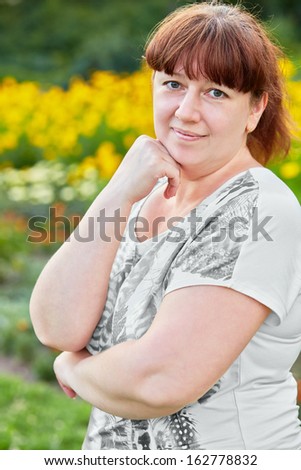 Half-length portrait of woman standing half-turned and propping head with hand against glade full of various flowers