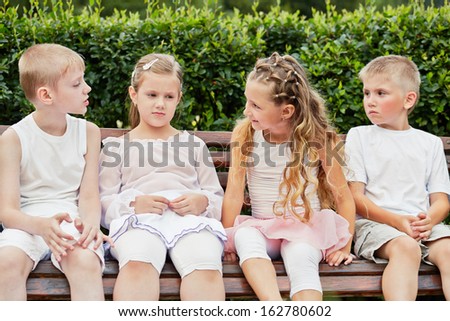 Four children sit on bench in summer park and talk about something