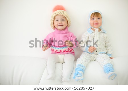 Two little kids in hats sit on back of white sofa at home. Shallow depth of field.