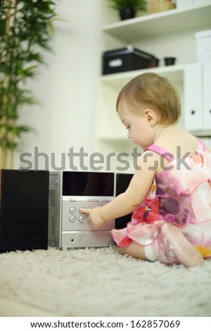 Little girl presses button on music system on carpet in room at home. Shallow depth of field.