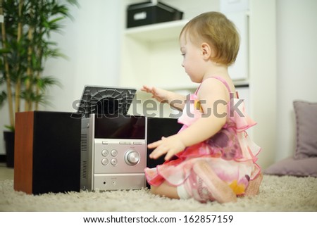 Little girl plays with music system on carpet in room at home. Shallow depth of field.