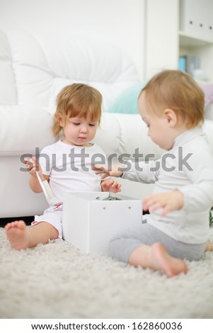 Two little girls sit on carpet and play with white box. Focus on left kid. Shallow depth of field.