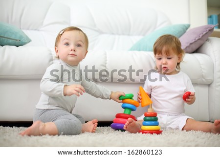 Two Little Kids Sit On Carpet And Play With Pyramids Near Sofa. Focus On Left Kid. Shallow Depth Of Field.
