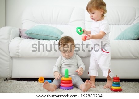 Two little kids on carpet play with pyramids near sofa. Focus on left kid. Shallow depth of field.