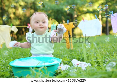 The little girl washes clothes in a small green basin near the rope with drying clothes