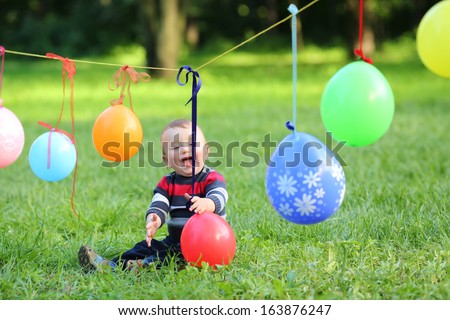 Little boy is playing with colorful balloons, which is tied to a rope in the park