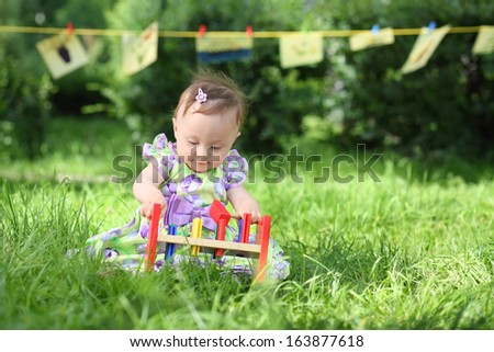 A little girl is playing with colorful wooden toys on the grass, in the background hanging kids drawings