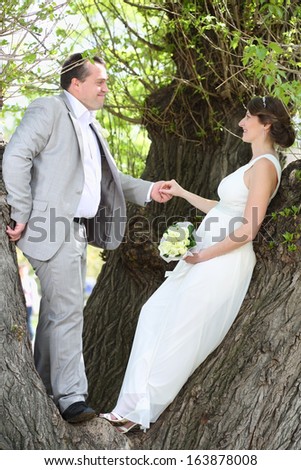 Beautiful newly married couple standing holding hands on a tree in the park
