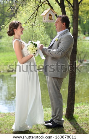 Beautiful bride and groom standing in a park holding hands and looking at each other, focus on the groom