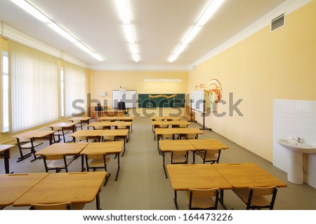 Empty classroom with wooden desks, chalk board and yellow walls in school.
