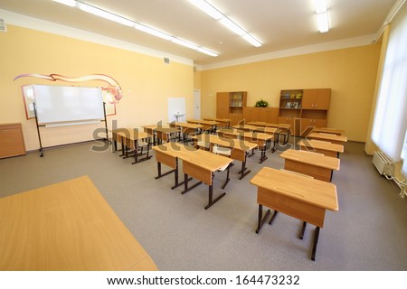Empty classroom with wooden desks, white chalk board and bookcases in school.