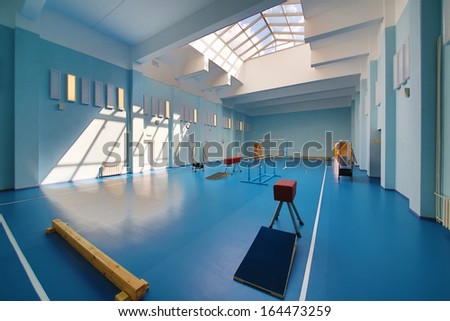 Empty school gymnasium with blue floor and exercise equipment.