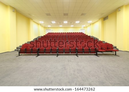 Small empty concert hall with red armchairs and yellow walls.