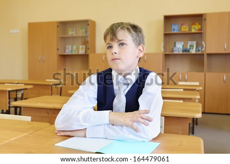 Boy sits at desk in classroom and listens attentively to teacher in school.