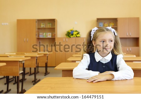 Little girl in school uniform sits at school desk and looks away in classroom in first grade for her alone.