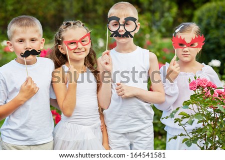 Children with masks on stiks stand together in summer park
