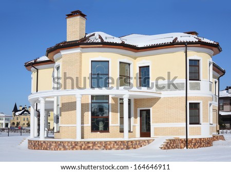 Roundish two-storey new cottage with columns on sunny frosty winter day.
