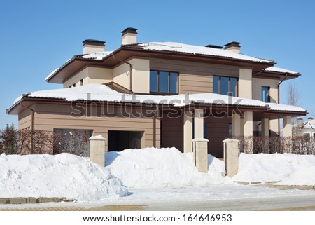 Simple brown cottage with garage at frosty and sunny winter day.