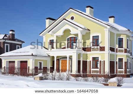 Facade of two-storey new cottage with garage at frosty and sunny winter day.