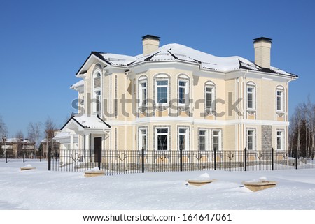 Two-storey light cottage with fence at frosty and sunny winter day.