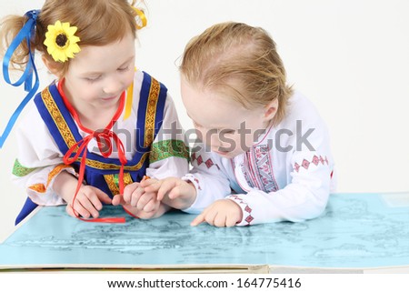 Little boy and girl in Russian folk costumes look at big map on white background.