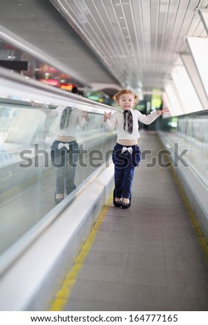 Little funny cute girl in mother shoes walks at long travelator.