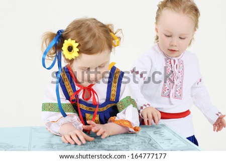 Little boy and girl in Russian national costume look at big map on white background.