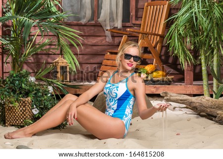 Beautiful girl in a swimsuit sunbathing on a sandy beach and throws sand
