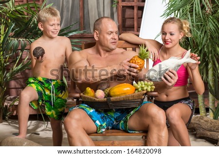 A family of three on a sandy beach with a basket of fruit and fish in fathers hand