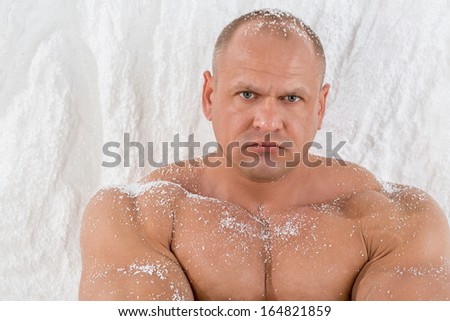 A strong man with big muscles with snow on body in studio with snow wall