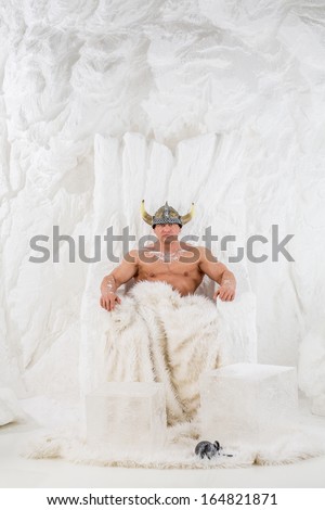 A muscular man in viking helmet  with snow on body sitting in snow chair