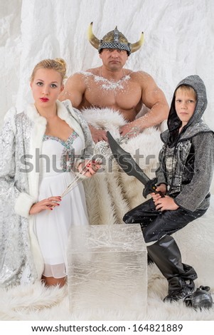 Family of three in historical costume viking with sword and helmet in studio with snow wall
