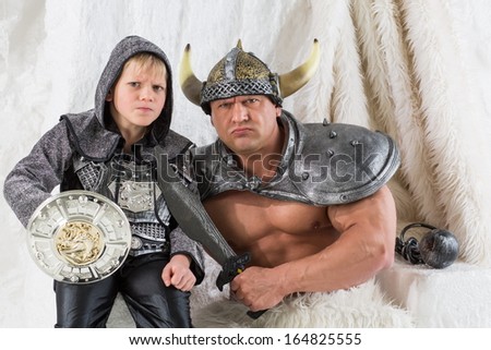 A muscular man with young son in costume viking with a sword with menacing faces