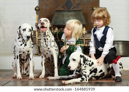 Two little boys in medieval costumes sit with three dalmatians near fireplace.