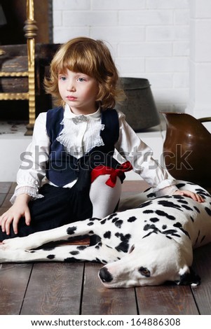 Serious pretty little boy in medieval costume sits with dalmatian near fireplace.