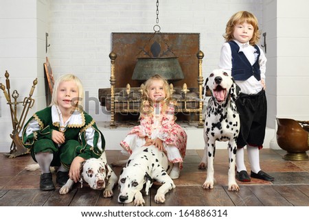Two happy boys and little girl in medieval costumes with three dalmatians sit near fireplace.