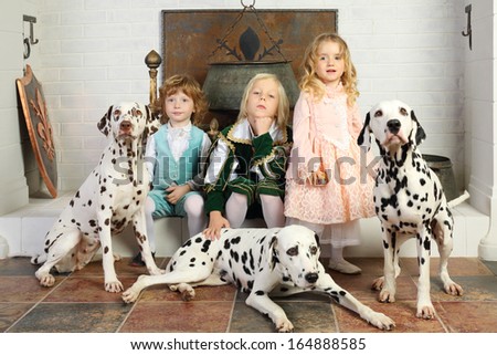 Two boys and girl in medieval costumes rest near fireplace with hanging pot with dalmatians.