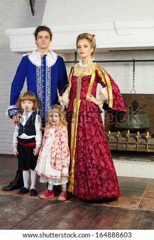 Father, mother, little daughter and son in medieval costumes stand near fireplace.