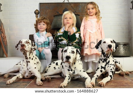 Two boys and little cute girl in medieval costumes and dalmatians sit near fireplace with hanging boiler.